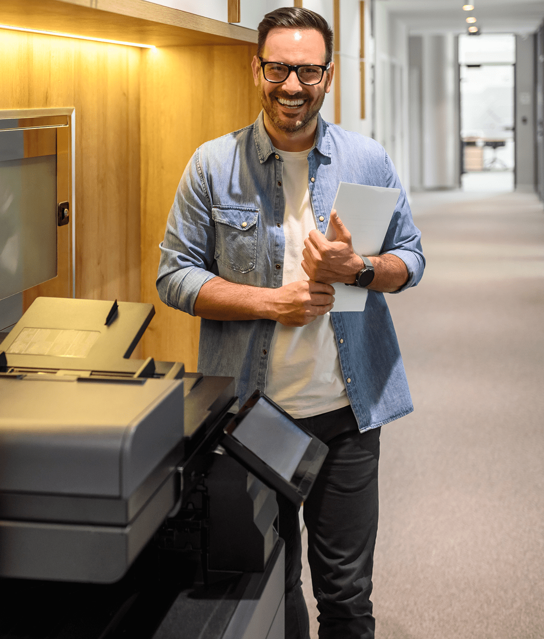 Man smiling near office printer, holding papers.